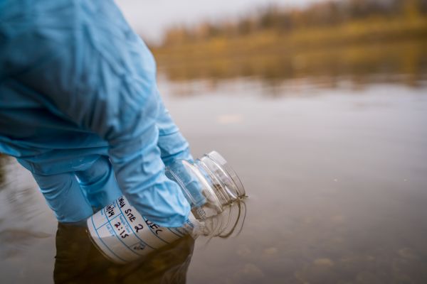 picture of sample bottle held in a blue gloved hand at river surface