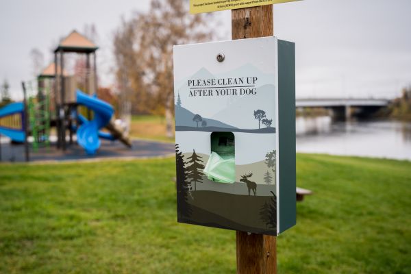 picture of box holding dog poop scoop bags on fence post near playground