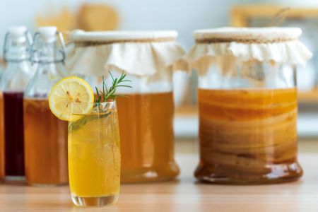 Glass of lemon-flavored kombucha with fermentation jars in the background